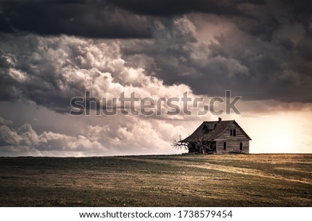 Old wooden farmhouse in the countryside at sunset with storm  clouds in the sky. There is a short grass meadow around the house. Royalty-Free Stock Photo #1738579454