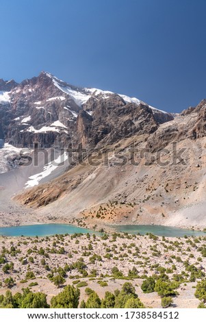The beautiful mountain trekking road with clear blue sky and rocky hills and fresh mountain lake in Fann mountains in Tajikistan