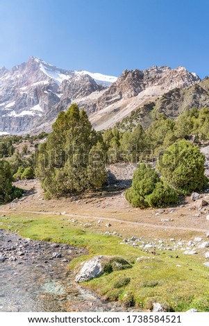 The beautiful mountain trekking road with clear blue sky and rocky hills and fresh mountain stream in Fann mountains in Tajikistan