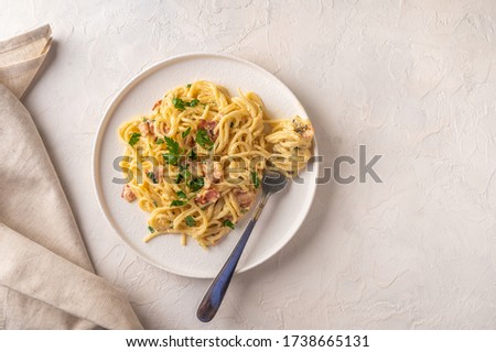 Classic homemade pasta carbonara Italian with bacon, eggs, parmesan cheese on light ceramic plate with fork and napkin on light table. Copy space