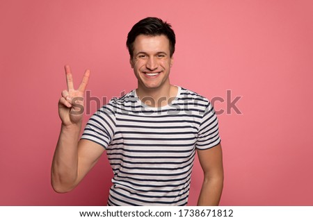 Make love, not war.Close-up photo of an optimistic man in a striped t-shirt, who is looking in the camera, smiling and showing a peace sign.