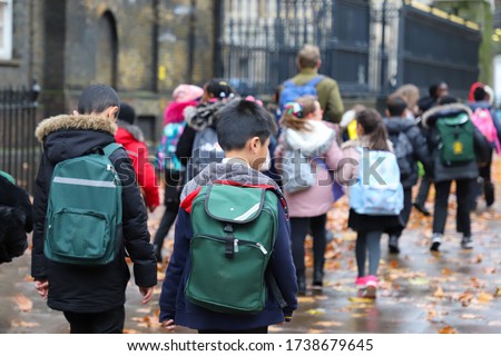 Multi-Cultural Children (asian, Indian, Chinese, Caucasian) primary student or kids and teacher carrying  school bag walk in street in rain winter day, with maple leaves on ground. back view Royalty-Free Stock Photo #1738679645