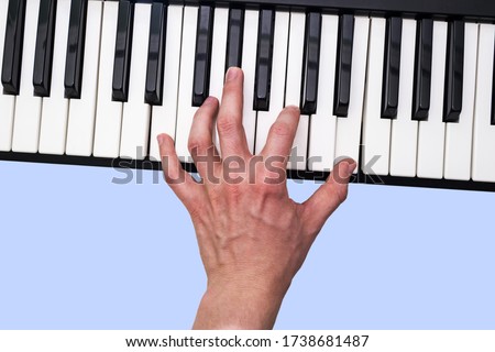 Close-up of a musical artist's hand playing on a synthesizer keyboard. Blue background.