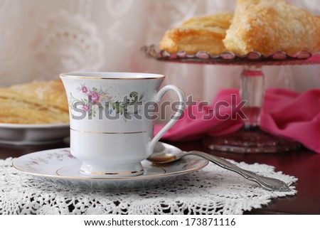 Elegant still life of beautiful vintage teacup and saucer with sweet pastries on pedestal plate in background. Closeup with shallow dof.