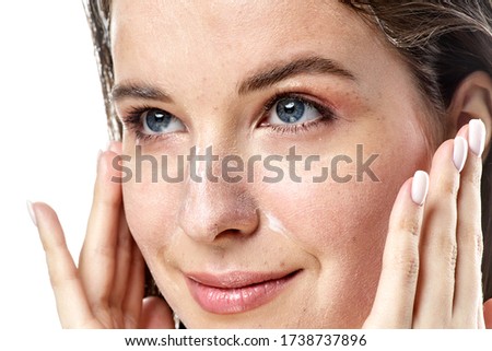 a close-up portrait of a young brunette girl with blue eyes with clear skin who applies cream to the face, isolated on a white background. High-resolution photos