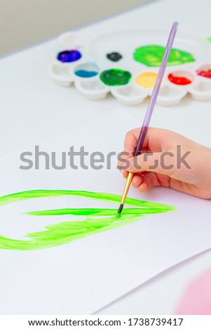 Close up of hand of child is drawing green leaf with brush by watercolors on white paper. Earth day concept.