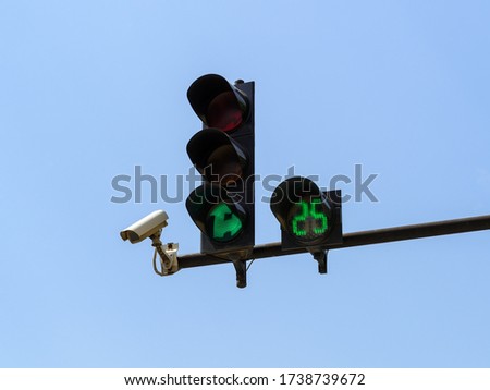 Green traffic light with digital timing countdown and traffic security camera surveillance (CCTV) against blue sky. Modern automatic traffic control. Close-up. Royalty-Free Stock Photo #1738739672