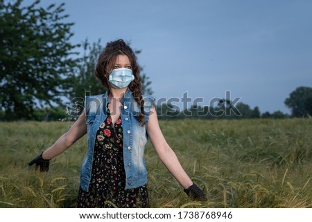 beautiful young woman wearing a surgical mask outdoor in a wheat field 