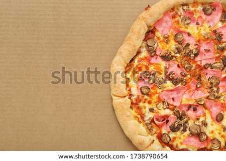 Pizza with mozzarella cheese, ham, onions, bacon, champignons, on brown corrugated fiberboard background.