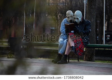 a date between two lovers during a virus epidemic, people in gas masks and respiratory masks during quarantine protect their respiratory organs from infection, sit on a Park bench and read a book Royalty-Free Stock Photo #1738808042