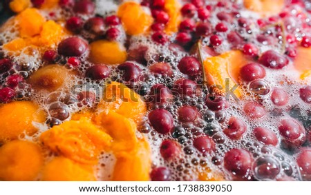 Fresh fruits are boiled in boiling water in a metal pan on a stove with bubbles and foam close-up. Cooking a delicious compote of apricot, apples, cherries, raspberries. Photography, concept.