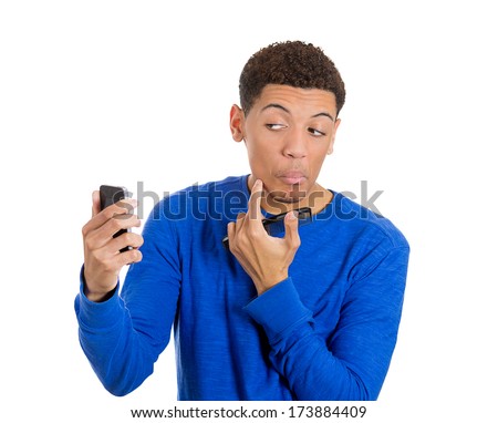 Closeup portrait of narcissistic handsome man in blue shirt looking admiring self in mirror cell phone finding spot on face, isolated on white background. Negative human emotions facial expressions.