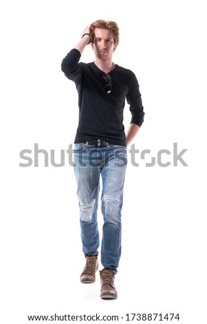 Confident red haired male fashion model walking and looking at camera touching hair style. Full body length isolated on white background. 