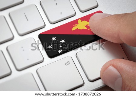 Online International Business concept: Computer key with the Papua New Guinea on it. Male hand pressing computer key with Papua New Guinea flag.