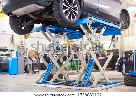 Lifted car without wheel waiting for repair in service station. Working area with automobile on high lift at vehicle repair shop. Concept of service center in process of car maintenance. Royalty-Free Stock Photo #1738880102