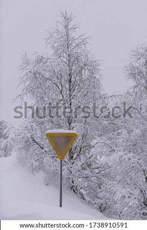 Snow covered yellow road sign in wintry setting