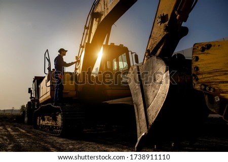 Sunset on the construction site. Silhouette of a contractor builder is sitting near bulldozer. Construction machinery concept Royalty-Free Stock Photo #1738911110