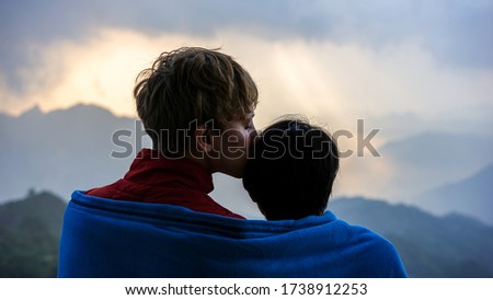 A young beautiful international couple, a love kiss in the forehead, partner is kissing a girl, watching sunrise in the mountains together, romantic young people travelling together, innocence passion