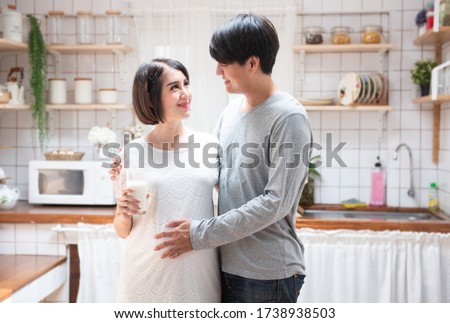 Portrait beautiful young asian couple pregnant woman drink milk dad embracing mom in kitchen. health care and love of pregnancy mother’s day concept. Royalty-Free Stock Photo #1738938503