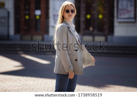 Sunny lifestyle fashion portrait of a young stylish hipster woman walking in city, wearing a fashionable outfit. Looking at camera. Walk in early autumn