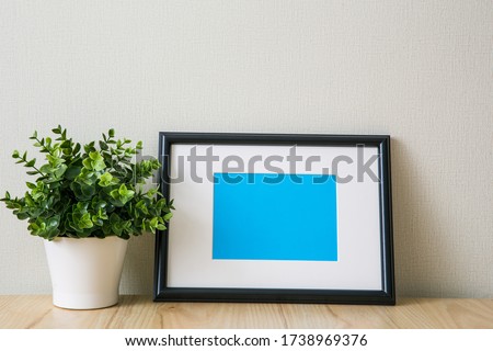 Mockup of a black horizontal photo frame with Passepartout. The light interior in the Scandinavian style. Composition on the table, shelf. Green plant in a white pot