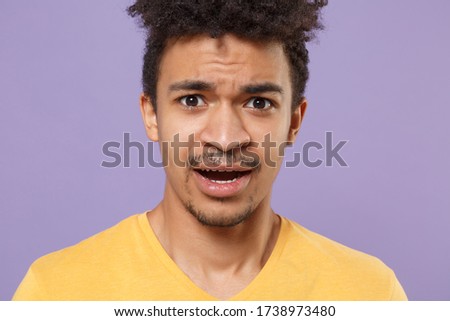 Close up of perplexed young african american guy in casual yellow t-shirt posing isolated on pastel violet background studio portrait. People lifestyle concept. Mock up copy space. Looking camera