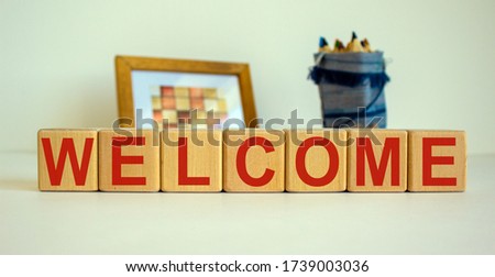 Wooden cubes with the inscription 'welcome'. Frame with a picture and a bag with pencils in the background. Beautiful white background, copy space.