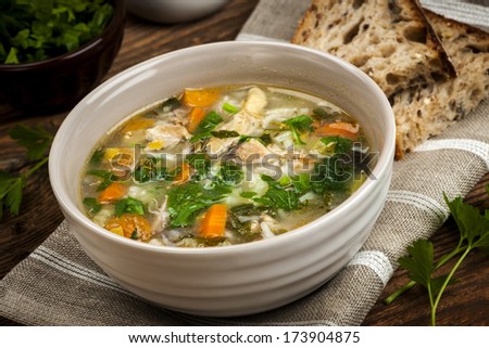 Chicken rice soup with vegetables in bowl and bread on rustic table
