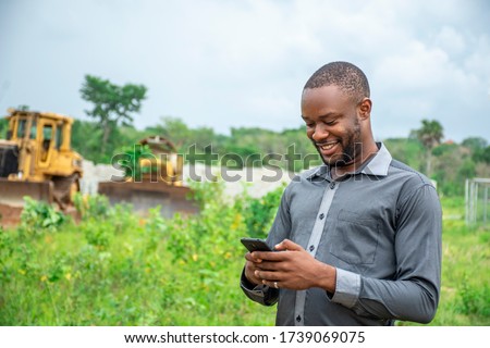 african agricultural businessman, using a mobile phone on a plot of land Royalty-Free Stock Photo #1739069075