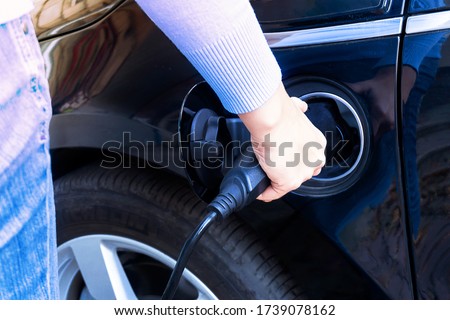 Woman charging modern electric car battery. Power plug plugged into an electric vehicle being charged for hybrid auto. Time for new vehicle fuel. Royalty-Free Stock Photo #1739078162