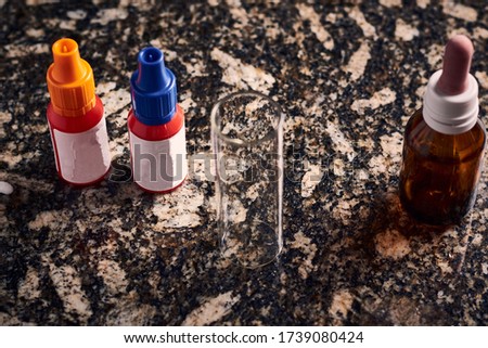 A high angle shot of medicinal drops and a messuring cup on a stone surface