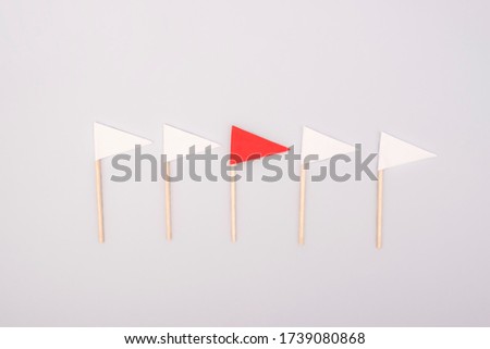 Red paper flag among white ones on gray background. Business concept.