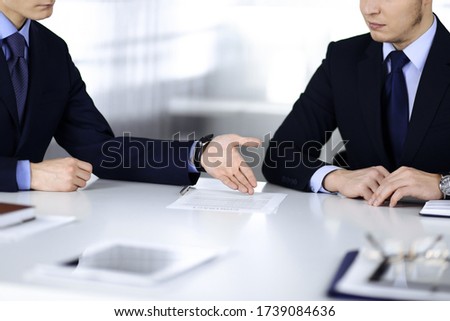 Business people discuss a contract, sitting at the desk in a modern office. Unknown businessman with a colleague, lawyers at negotiation. Teamwork and partnership concept
