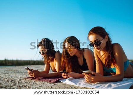 Three beautiful  girls using mobile smart phone at the beach. Girls sunbathing on the beach. Young girls doing selfie with phone. Enjoy summer time.