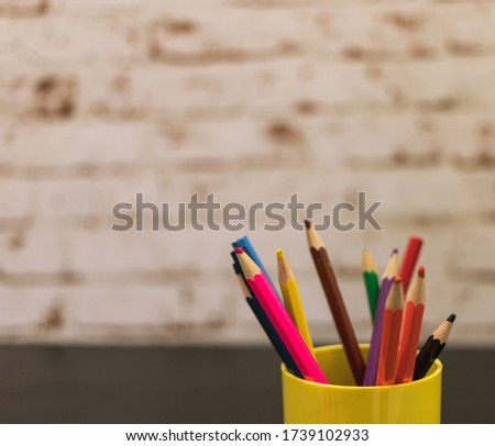 a few colored pencils. pencils of different colors. colored pencils stand in a cup. The background is a brick wall painted. glass of yellow. pencils for children.