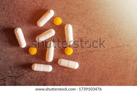 Yellow and white and red antibiotic pills from a jar on a dark concrete table