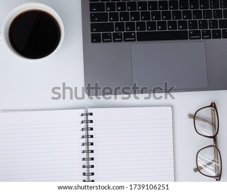 Flat lay, Office table white desk, Bright Creative workspace with eyeglasses, black pen, lab-top, a cup of black coffee, and blank notebook, Top view with copy space