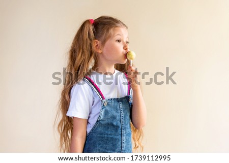 A little girl with ponytails kisses a round Lollipop on a stick.