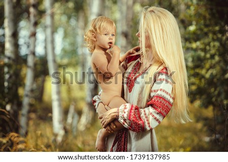A beautiful young mother with her little daughter in traditional old Slavic dress, posing in the open air. National embroidered pattern on the sleeve of a linen shirt. Pagan ancient symbols.
