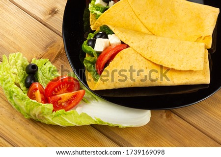 Vegetarian healthy corn tortillas, salad, tomatoes, olives on a wooden table. Selective focus.