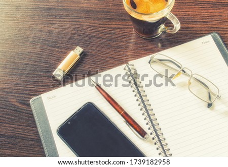 USB drive, cup of coffee, open notebook, mobile phone, pen and glasses on a table made of brown wood. Indoors. Horizontal format. Color. Photo.