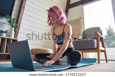 Young fit sporty teen hipster girl pink hair wear sportswear search online fitness yoga class using laptop computer sit at home. Online fitness workout video tutorial virtual coach teacher concept.