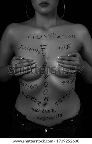 part of the body of a young girl with the inscription, humiliation, bullying, freedom, racism, violence . the captions are written in the photographer's hand, not in a tattoo . black and white photo.