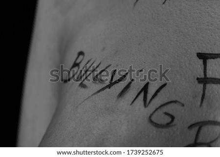 part of the body of a young girl with the inscription bullying . the captions are written in the photographer's hand, not in a tattoo . black and white photo.