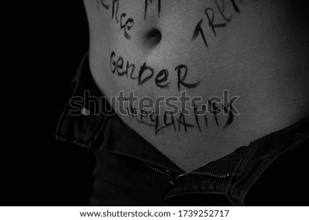 part of the body of a young girl with the inscription gender inequality . the captions are written in the photographer's hand, not in a tattoo . black and white photo.