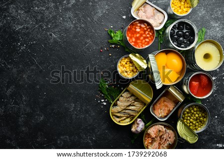 Canned vegetables, beans, fish and fruits in tin cans on black stone background. Food stocks. Royalty-Free Stock Photo #1739292068