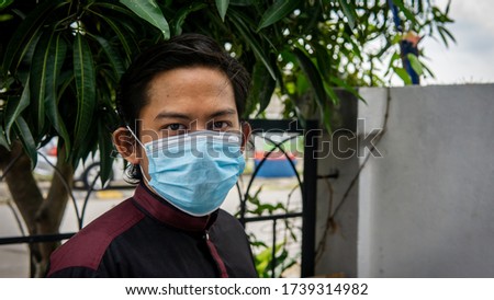 A portrait of young Asian Malay man with traditional Kurta shirt wearing a 3 layer face mask during the Eid al-Fitr celebration in Coronavirus season. Hygiene lifestyle. New normal concept.