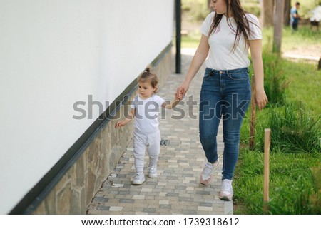 Cute little girl spend time with mom neae the house. Mother and daughter walk on the backyard