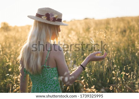 
blonde girl walking on the field touching the grass with hat at sunset