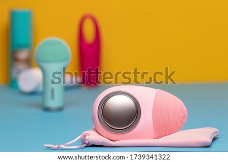 Beauty and skincare concept. Selective focus on a modern pink electric face cleansing silicone brush with massage sonic vibration on a blue table and two further blurred electric beauty treatment devi